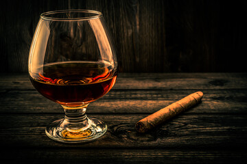 Glass of brandy and cuban cigar on a old wooden table. Focus on the glass of brandy