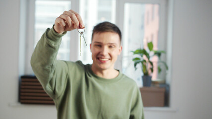 A young guy stands in a white empty room and shakes keys with a smile