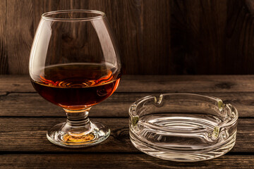 Glass of brandy and glass ashtray on a old wooden table