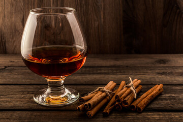 Glass of brandy with cinnamon sticks tied with jute rope on an old wooden table. Focus on the...