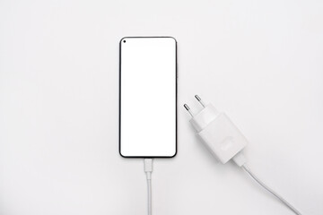 Smartphone with white screen mockup and power supply, phone charger on a white background. USB cable for wired charging of the phone battery. top view, flat lay, copy space for text