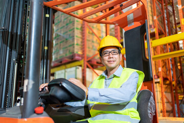 Forklift driver asian man in safety jumpsuit uniform with yellow hardhat at warehouse. Worker male...