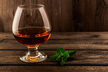 Glass of brandy with mint sprig on an old wooden table. Focus on the mint sprig