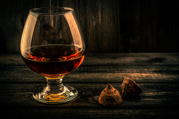 Glass of brandy and a couple of chocolate truffles on an old wooden table