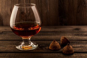 Glass of brandy and a chocolate truffles on an old wooden table. Focus on the chocolate truffles