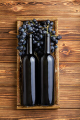 Two Red Wine bottles composition on brown wooden table. Red wine bottles in box on black ripe grapes on wooden table. Old collection wine label template Top view vertical