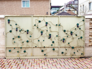 Light iron gate in a wrought-iron pattern in the form of a vine in front of a private house