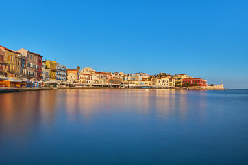 View of old port of Chania of Crete island Greece. Restaurants on the quay in the morning sun with reflections in the polished water in the foreground. Bay of Xania at sunny summer day. The harbour of