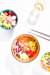 Differetn Poke bowls  with vegetables and salmon o,tuna, edamame beans, on n a white  background with chopstick and a glass of white whine, top view ,flatlay with directionl light and defined shadow