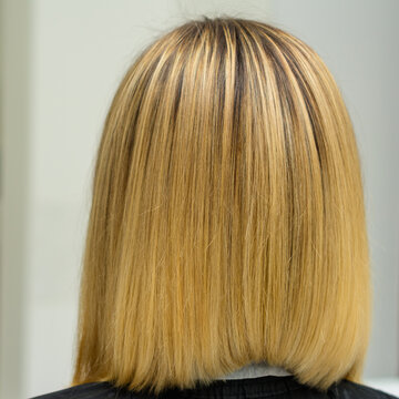 Female hairdresser holds in hand between fingers blond hair, comb and scissors close up, straightening hair tips.
