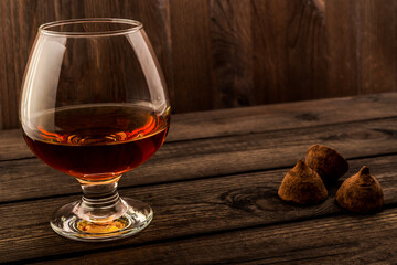 Glass of brandy and a chocolate truffles on an old wooden table. Angle view, focus on the glass of brandy