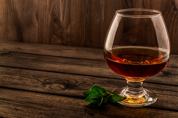 Glass of brandy with mint sprig on an old wooden table. Angle view