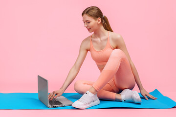 Obraz na płótnie Canvas young sportive woman doing workout with laptop, on pink background, Fitness training online