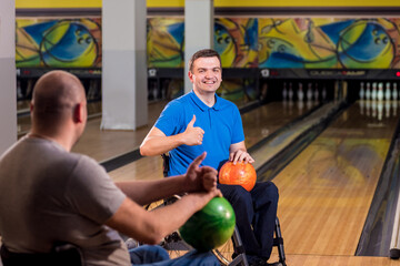 Two young disabled men in wheelchairs playing bowling in the club