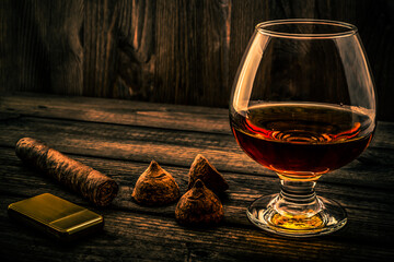 Glass of brandy and a couple of chocolate truffles with cuban cigar and golden lighter on an old...