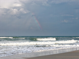 Calmful ocean beach dusk sunset with rainbow in deep blue sky and breezing waves.