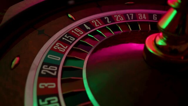 Rotating roulette wheel close up in the rays of purple neon lights. The small white ball hits red 14, the bet wins. Part of the roulette wheel runs in slow motion.