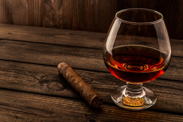 Glass of brandy and cuban cigar on an old wooden table. Angle view