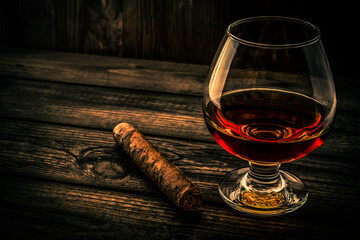 Glass of brandy and cuban cigar on an old wooden table. Angle view