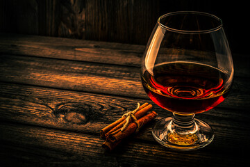 Glass of brandy with cinnamon sticks tied with jute rope on an old wooden table. Angle view