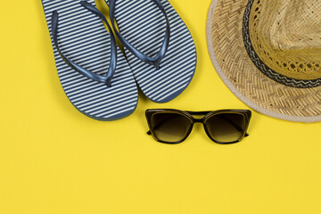 Summer background. Straw sun hat, sunglasses and beach striped flip flops on a yellow background. Top view, close-up, horizontal. Summer concept. Copy space.