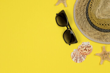 Summer background. Straw sun hat, sunglasses and seashells on a yellow background. Top view, close-up, horizontal. Summer concept. Copy space to the left.