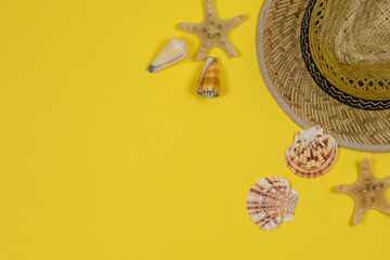 Summer background. Straw sun hat and seashells on a yellow background. Top view, close-up, horizontal. Summer concept. Copy space to the left.