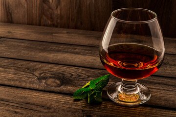 Glass of brandy with mint sprig on an old wooden table. Angle view