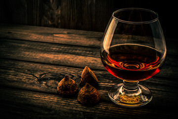 Glass of brandy and a chocolate truffles on an old wooden table. Angle view