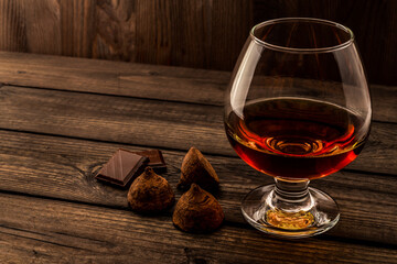 Glass of brandy and a chocolate truffles with chocolate on an old wooden table. Angle view