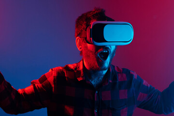 young man hallucinating and enjoying an immersive experience with virtual reality technology. Portrait in studio with colored lights. Amazed person with VR glasses.