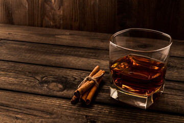 Glass of brandy with cinnamon sticks tied with jute rope on an old wooden table. Angle view