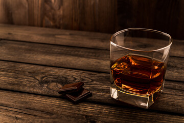Glass of brandy and a chocolate on an old wooden table. Angle view