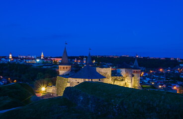 View on the Kamianets-Podilskyi ?astle in the evening. Beautiful stone castle on the hill on the sunset. Clouds in the darkening sky above the castle. Blue hour. Ukraine