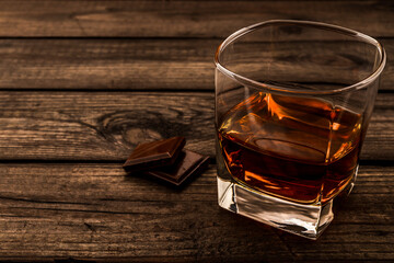 Glass of brandy and a chocolate on an old wooden table. Focus on the glass of brandy, close up view