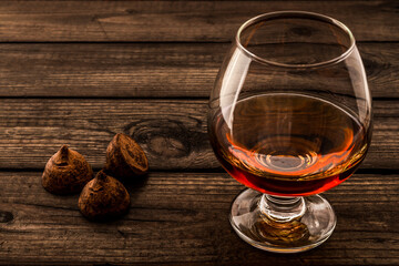 Glass of brandy and a chocolate truffles on an old wooden table. Close up view