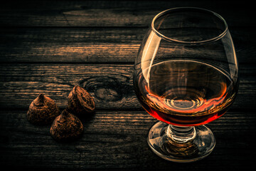 Glass of brandy and a chocolate truffles on an old wooden table. Close up view