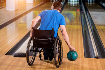 Young disabled man in wheelchair playing bowling in the club