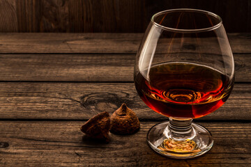 Glass of brandy and a couple of chocolate truffles on an old wooden table. Angle view