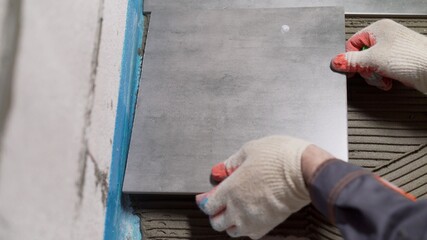 Process of laying ceramic tiles on floor smeared with glue. Workers hands with a tile close up. The process of laying ceramic tiles on the floor.