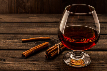 Glass of brandy with cinnamon sticks tied with jute rope on an old wooden table. Angle view