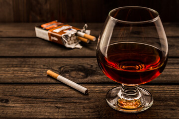 Glass of brandy and cigarette with pack of cigarettes on a old wooden table. Angle view