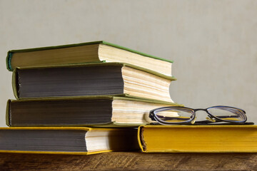 On wooden table is stack of old books with colorful covers and glasses. Close-up. Copy space. Selective Focus.