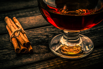Glass of brandy with cinnamon sticks tied with jute rope on an old wooden table. Close up view