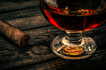 Glass of brandy and cuban cigar on an old wooden table. Close up view