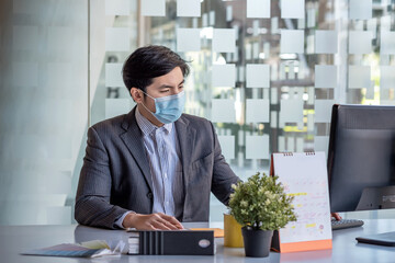 Asian businessman working on a computer while wearing a mask at the office.