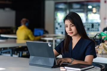 Front view of a beautiful Asian businesswoman sitting in the office working on a tablet.