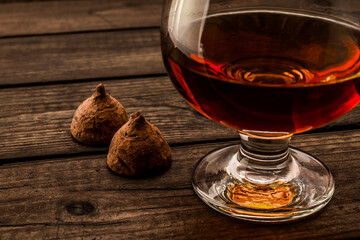Glass of brandy and a couple of chocolate truffles on an old wooden table. Close up view