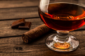 Glass of brandy and a chocolate with cuban cigar on an old wooden table. . Close up view, shallow depth of field