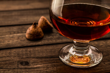 Glass of brandy and a couple of chocolate truffles on an old wooden table. Close up view, shallow depth of field, focus on the glass of brandy